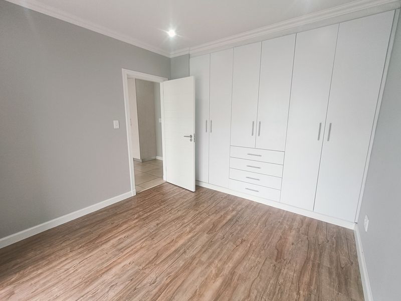 A bright, modern bedroom featuring neutral grey walls, high-quality laminate flooring, and extensive floor-to-ceiling built-in cupboards for ample storage.