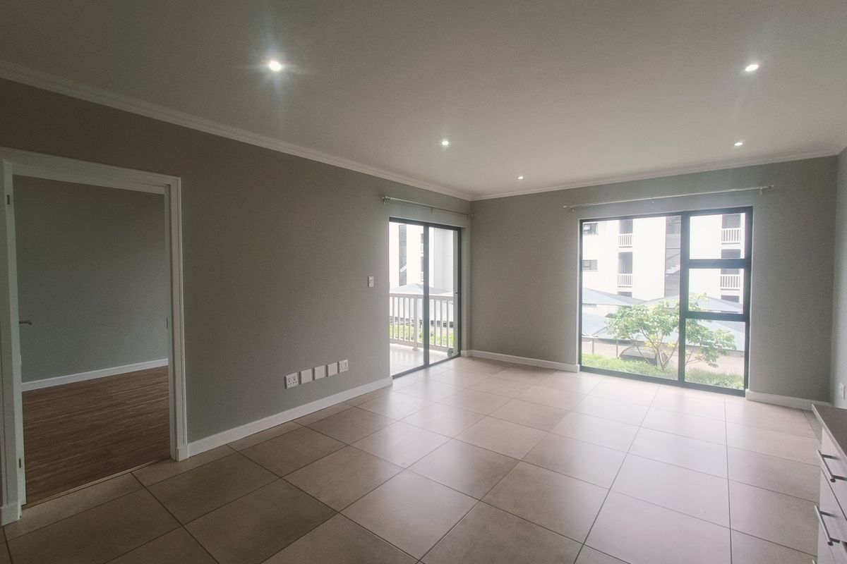A spacious, empty living area featuring neutral tiled flooring, recessed downlights, and large sliding glass doors leading to an outdoor balcony.