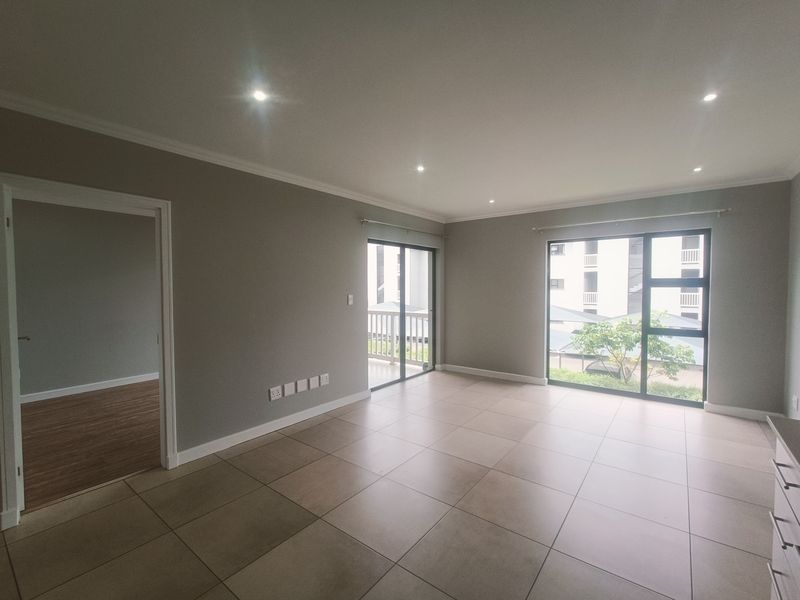 A spacious, empty living area featuring neutral tiled flooring, recessed downlights, and large sliding glass doors leading to an outdoor balcony.