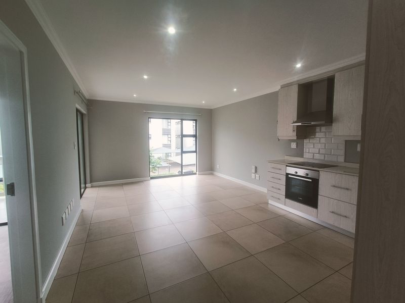 Modern open-plan living area featuring a sleek kitchen with built-in appliances, tiled flooring, and abundant natural light from large sliding glass doors.