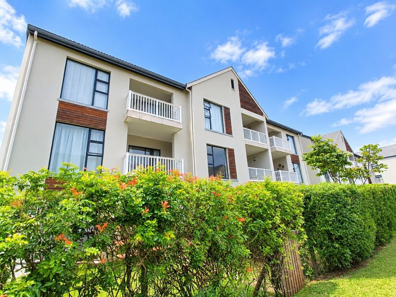 A low-angle view of a modern apartment complex facade featuring multiple balconies, timber accents, and well-maintained landscaped hedges.