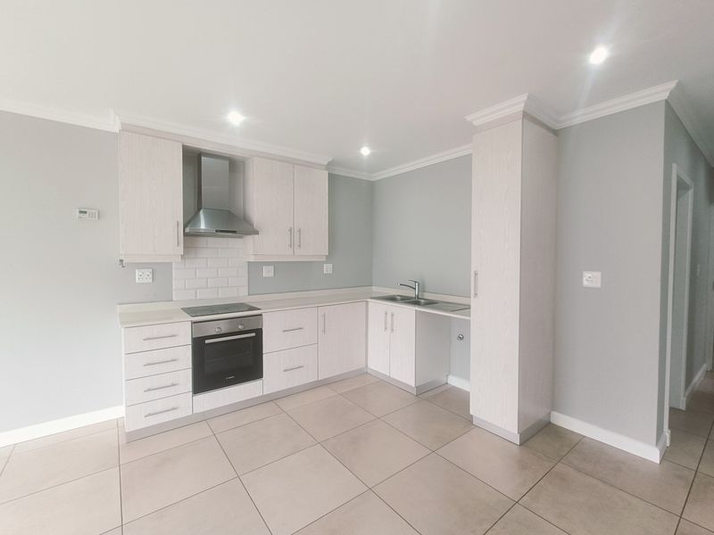A modern, clean kitchen featuring light wood cabinetry, a built-in oven and hob, subway tile backsplash, and neutral tiled flooring in an open-plan layout.