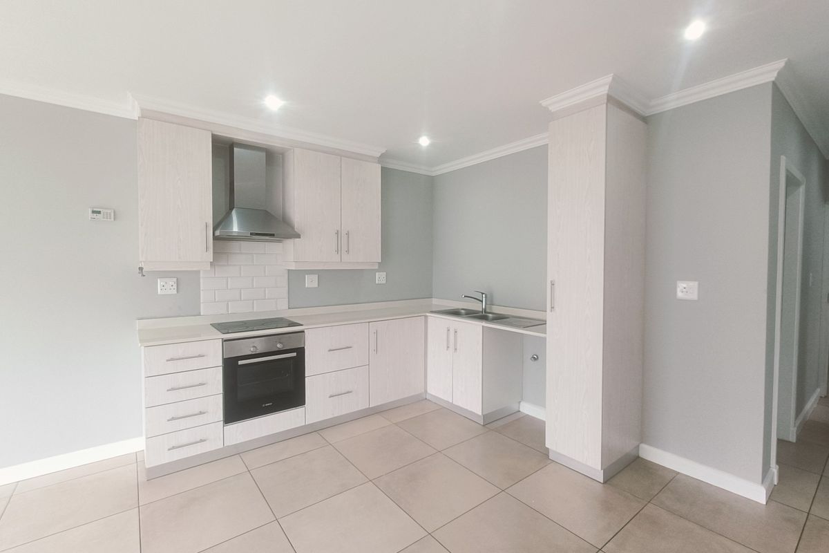 A modern, clean kitchen featuring light wood cabinetry, a built-in oven and hob, subway tile backsplash, and neutral tiled flooring in an open-plan layout.