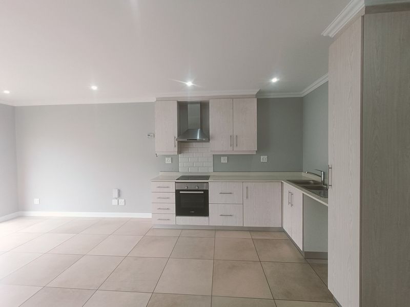 A modern open-plan kitchen featuring light wood cabinetry, integrated appliances, subway tile backsplash, and neutral tiled flooring in a clean, well-maintained space.