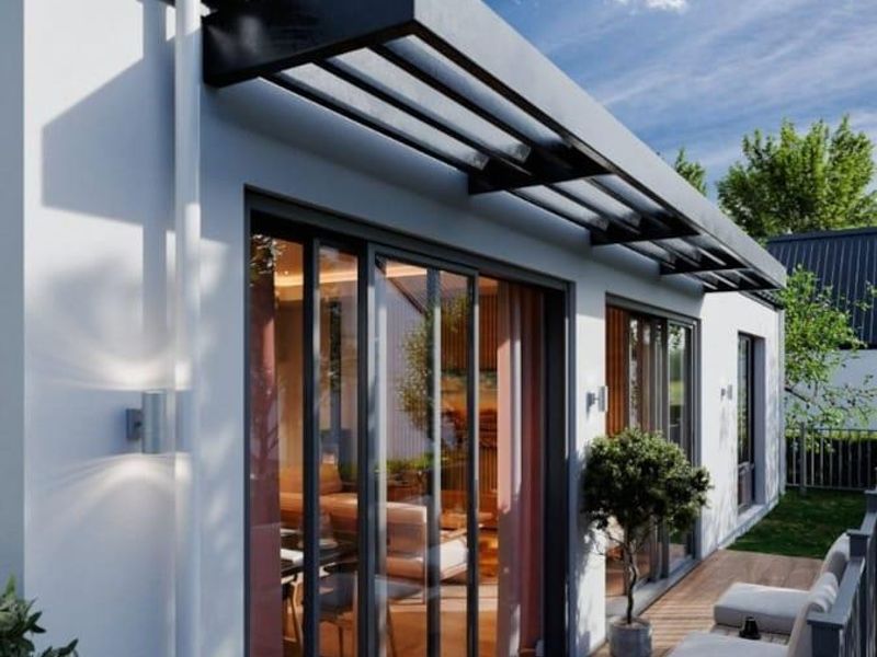 A modern, well-maintained timber deck patio featuring a fixed overhead canopy, sliding glass doors, and contemporary exterior lighting.