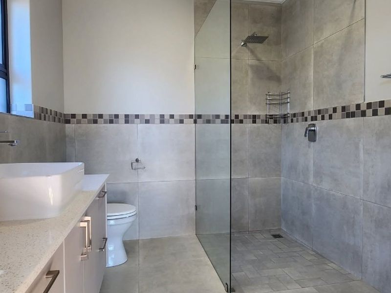 Modern bathroom featuring a spacious walk-in shower with glass screen, contemporary vanity with countertop basin, and neutral floor-to-ceiling tiling.
