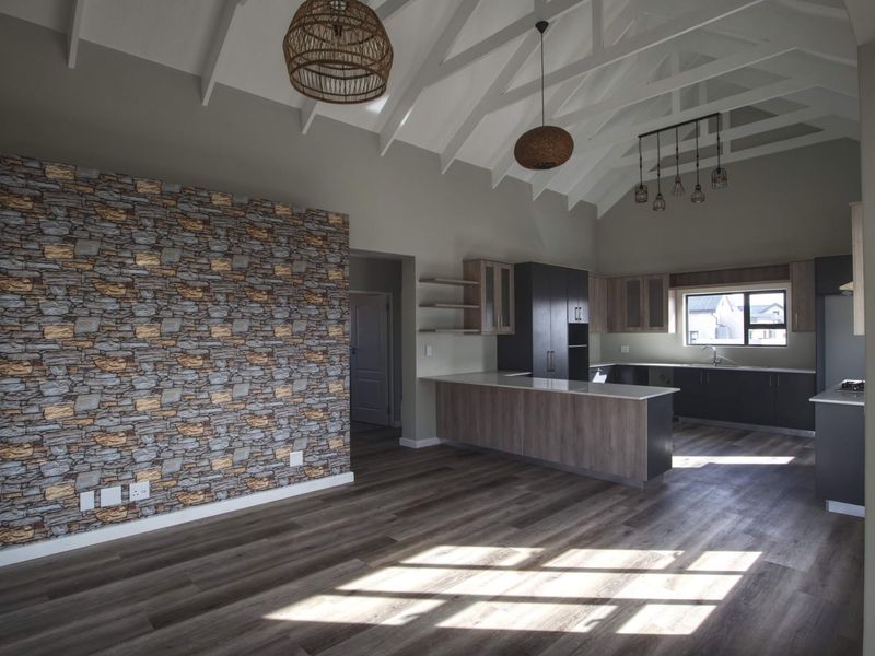 Spacious open-plan living and kitchen area featuring a vaulted ceiling with exposed rafters, modern cabinetry, a kitchen island, and a stone-look feature wall.