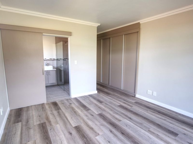 Spacious bedroom featuring modern laminate flooring, built-in cupboards, and direct access to an en-suite bathroom with contemporary finishes.