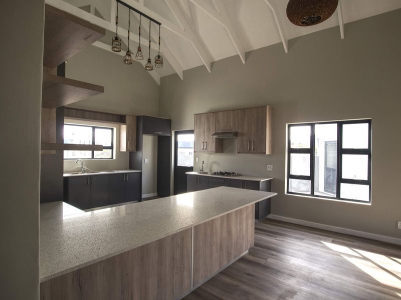 Modern open-plan kitchen featuring a large island with stone countertops, built-in cabinetry, gas hob, and high vaulted ceilings with exposed rafters.
