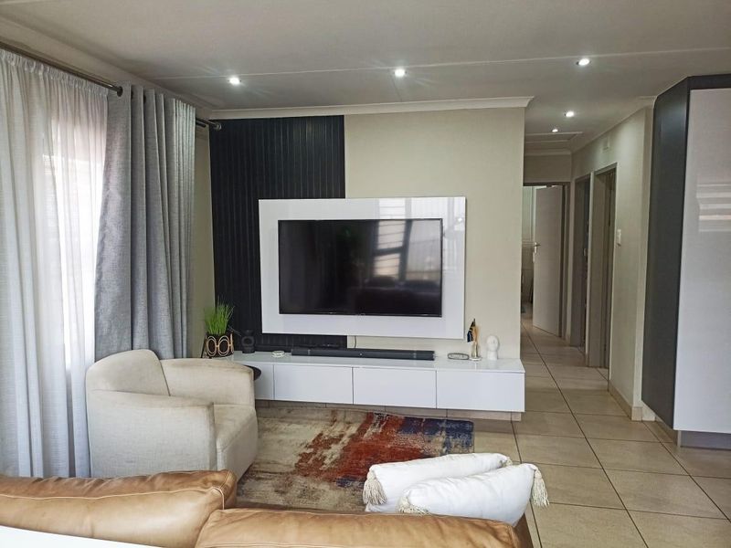 A well-maintained living room featuring a modern built-in media console, decorative feature wall paneling, recessed ceiling lighting, and neutral tiled flooring.