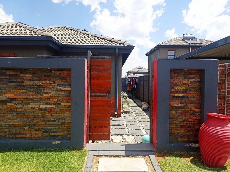 A well-maintained rear exterior area featuring a stone-clad boundary wall, timber gate, and a paved walkway leading between residential units.