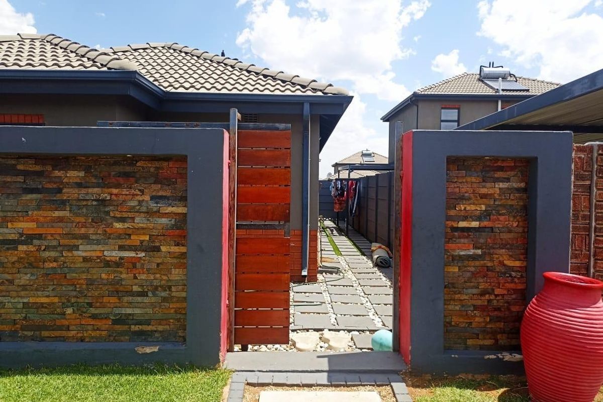 A well-maintained rear exterior area featuring a stone-clad boundary wall, timber gate, and a paved walkway leading between residential units.