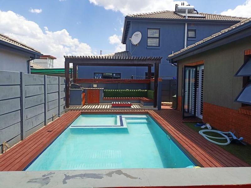 Outdoor entertainment area featuring a swimming pool with timber decking, a pergola, and a built-in braai station.