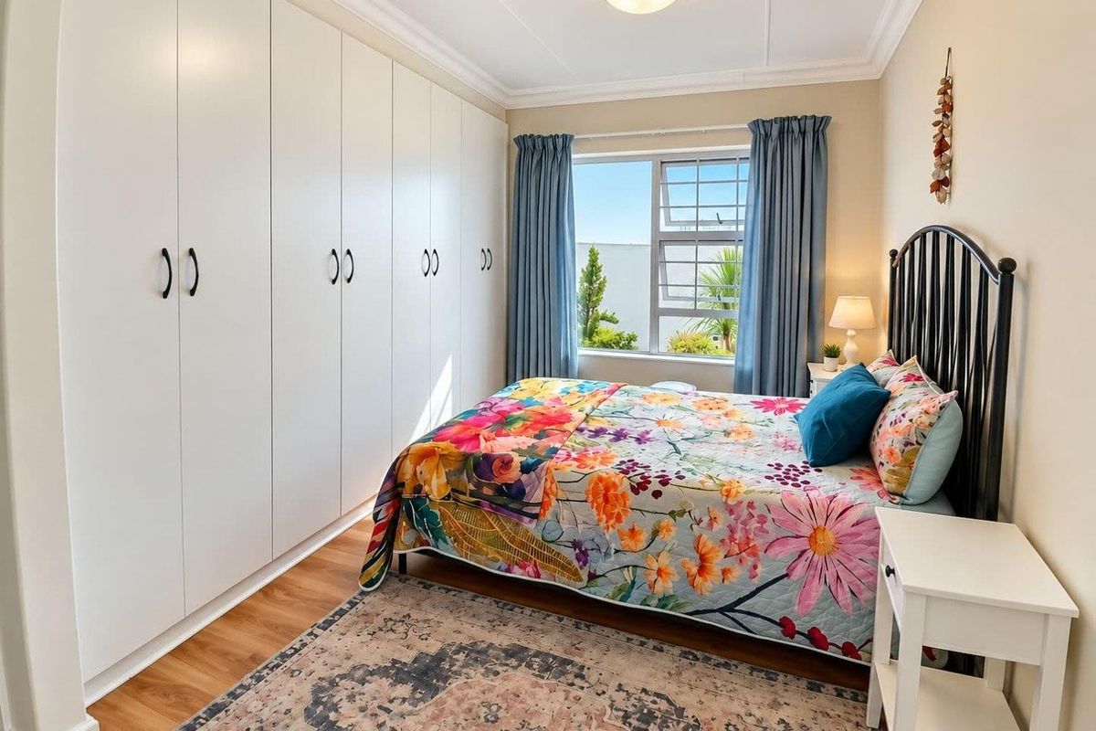 A well-maintained bedroom featuring extensive built-in cupboards, laminate flooring, and a large window providing natural light.