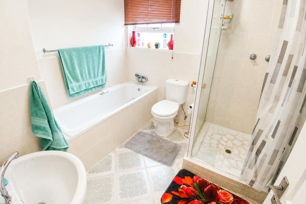 A functional bathroom featuring a built-in bathtub, separate shower enclosure, toilet, and pedestal basin with neutral wall tiling.