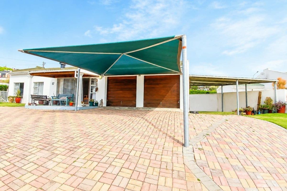 Front exterior view featuring a paved driveway, double garage doors, and a large shade sail structure providing covered parking.