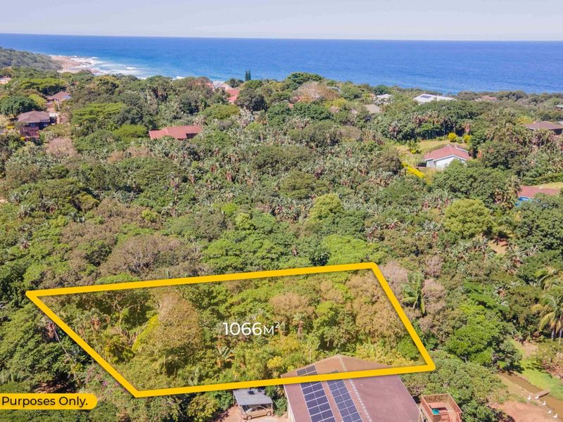 An aerial view of a 1066m2 vacant residential plot surrounded by lush coastal vegetation with ocean views in the background.
