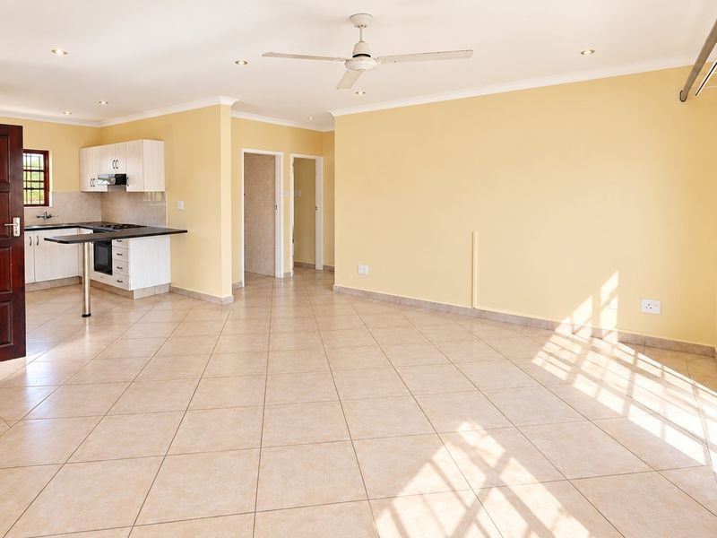 Spacious open-plan living area featuring tiled floors, a ceiling fan, and a functional kitchen with built-in cabinetry, oven, and breakfast bar.