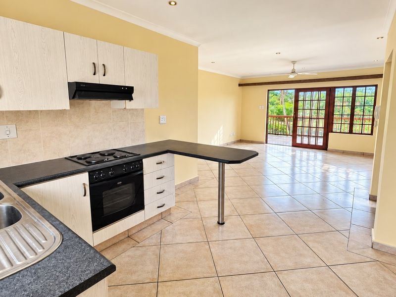 Spacious open-plan kitchen and living area featuring tiled floors, built-in cabinetry, and direct access to a balcony through sliding glass doors.