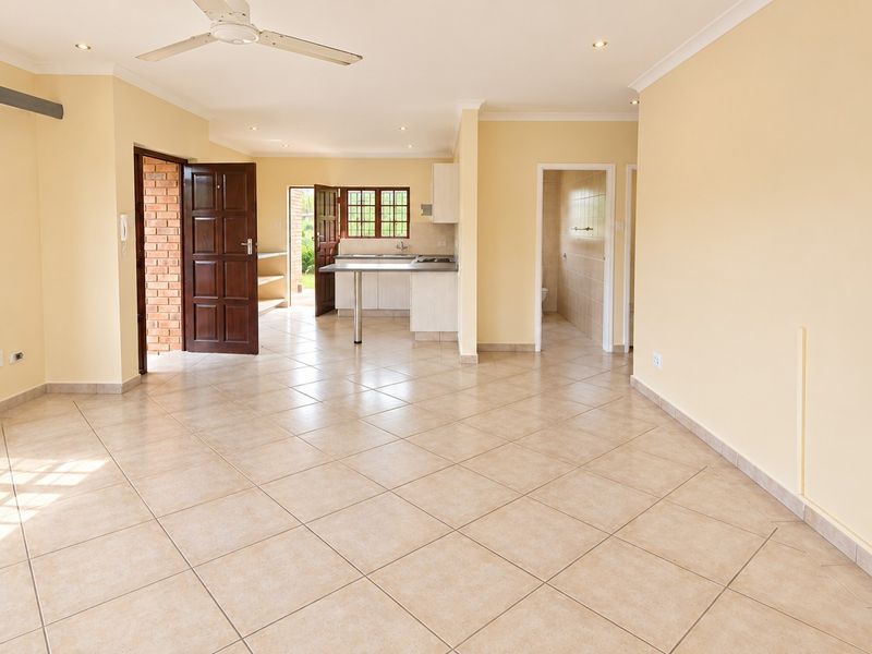 Spacious open-plan living area featuring tiled flooring, a ceiling fan, and an integrated kitchen with breakfast bar and ample cabinetry.