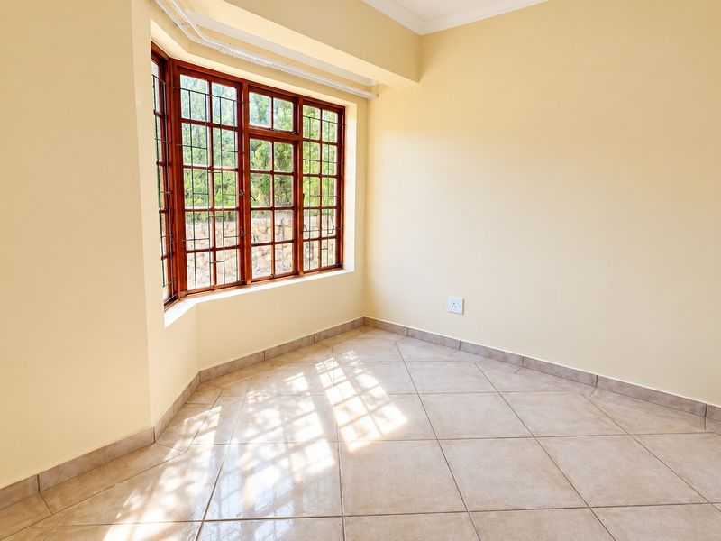 A bright, empty bedroom featuring large bay windows, neutral tiled flooring, and built-in wardrobe storage.