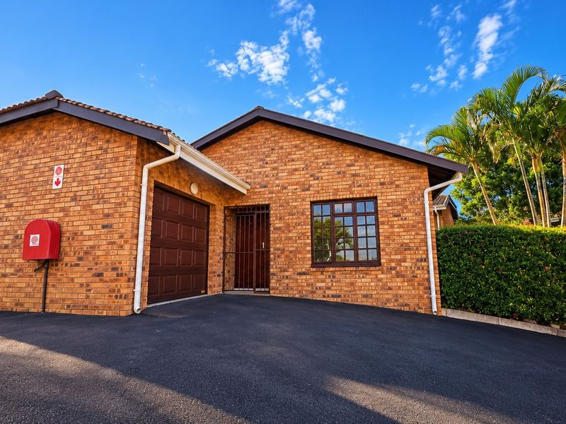 Front exterior view of a well-maintained face brick townhouse featuring a single garage, secure entrance, and paved driveway.