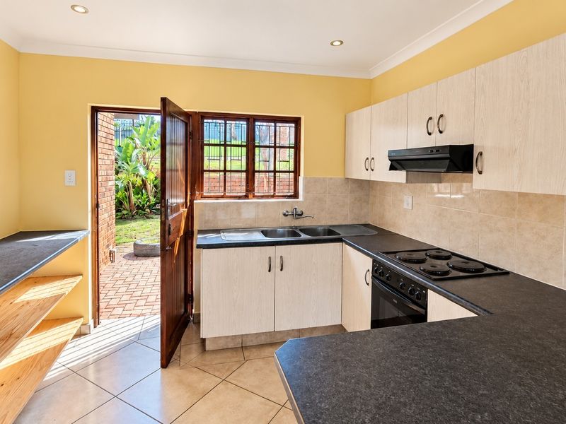 Functional kitchen featuring built-in cabinetry, laminate countertops, electric hob, oven, and direct access to the rear garden area.