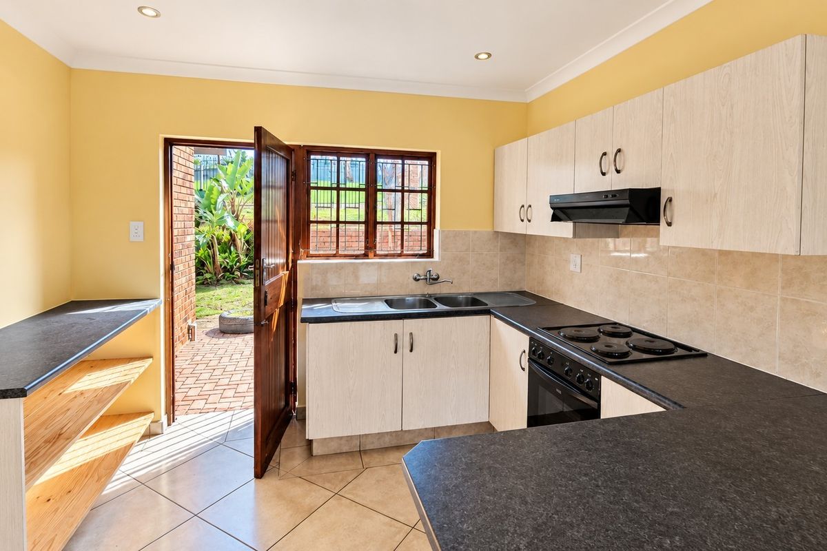Functional kitchen featuring built-in cabinetry, laminate countertops, electric hob, oven, and direct access to the rear garden area.