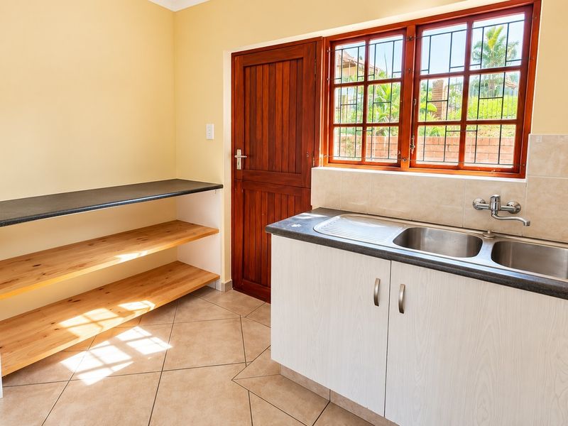A functional scullery or laundry area featuring a double stainless steel sink, laminate cabinetry, tiled flooring, and direct access to the exterior.