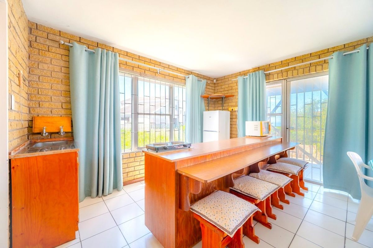 A functional kitchen area featuring exposed brick walls, tiled flooring, and a built-in breakfast bar with integrated seating, offering direct access to the outdoors.