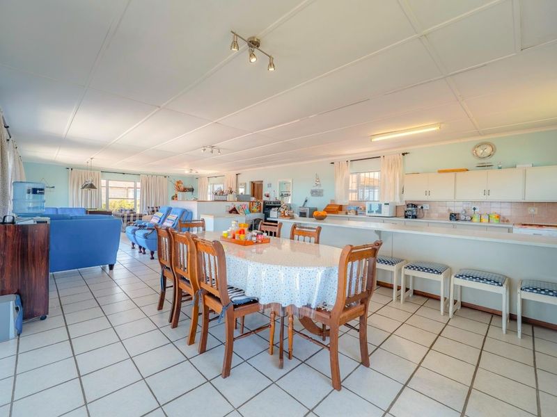 Spacious open-plan living and dining area featuring a functional kitchen with a breakfast bar, tiled flooring, and ample natural light.