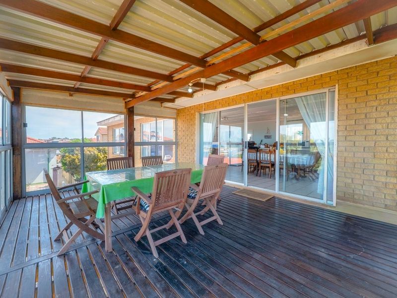 A covered outdoor patio featuring timber decking, exposed rafters, and sliding glass doors providing access to the interior living space.