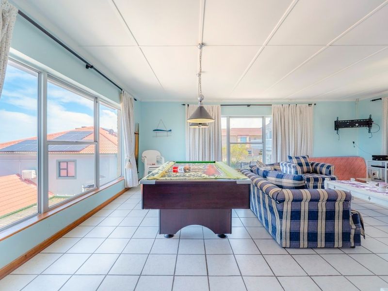 Spacious living area featuring large windows, tiled flooring, and a central pendant light, offering a bright and open space for relaxation and entertainment.