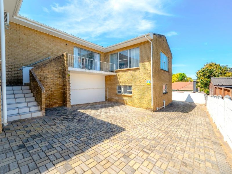 Rear exterior view of a double-story brick house featuring a paved driveway, external staircase leading to a balcony, and secure boundary walling.