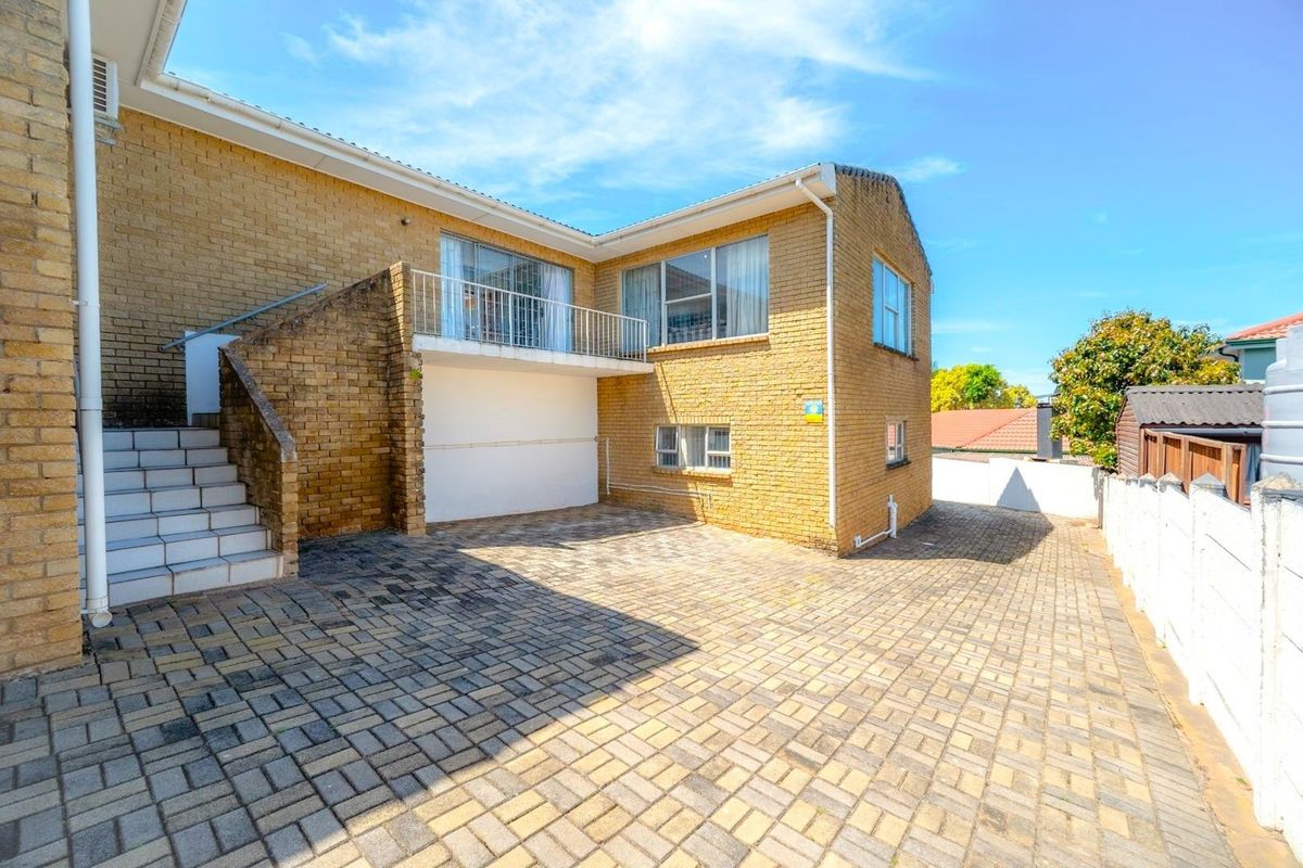 Rear exterior view of a double-story brick house featuring a paved driveway, external staircase leading to a balcony, and secure boundary walling.