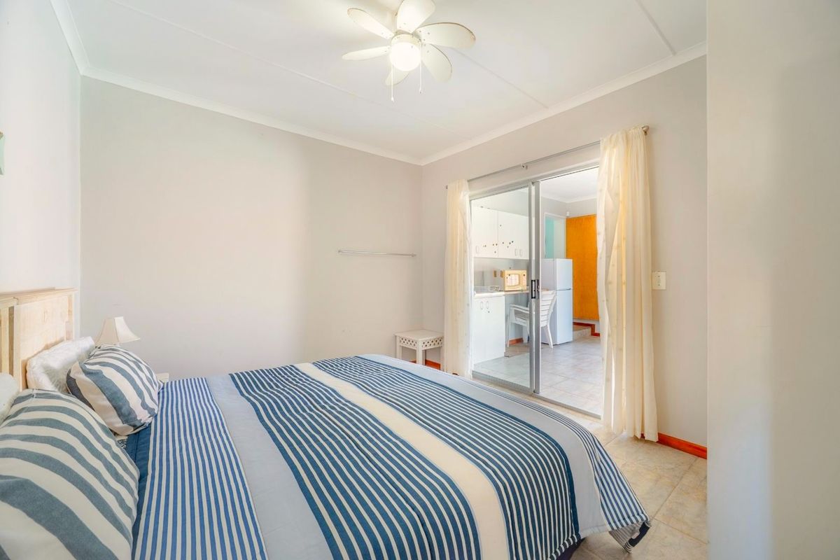 A bedroom featuring tiled flooring, a ceiling fan, and a sliding glass door providing access to an adjacent kitchen area.