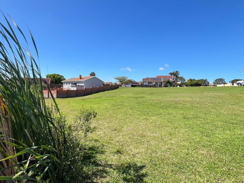 A wide, open residential plot featuring a well-maintained grass lawn and a brick boundary wall, situated in a quiet neighborhood setting.
