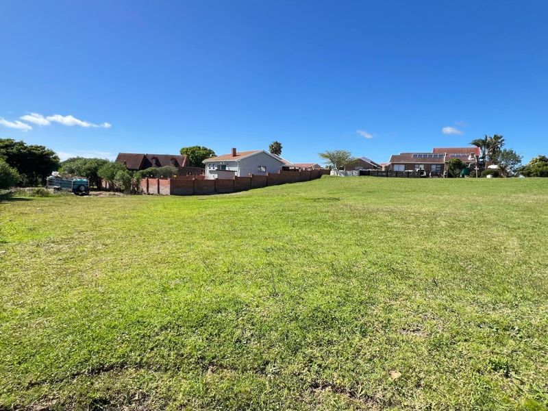 A wide-angle view of a vacant residential plot featuring a well-maintained grass lawn and surrounding boundary walls in a quiet neighborhood setting.