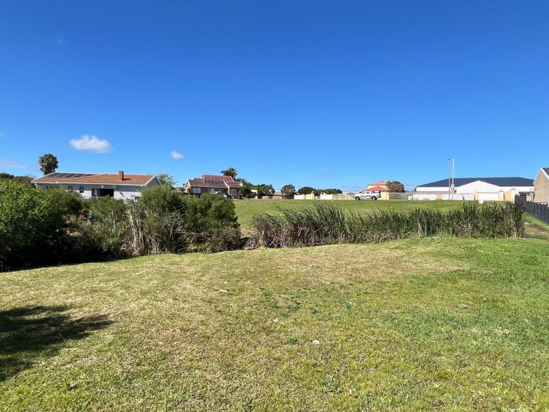 A view of a residential vacant land plot featuring a grass lawn and perimeter fencing, situated in a suburban neighborhood.