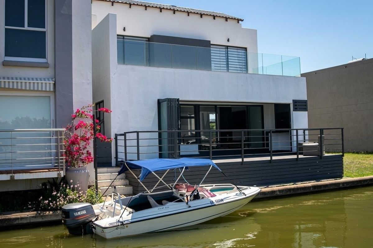 Modern waterfront residence featuring a spacious timber deck, glass balustrades, and large stacking doors providing seamless indoor-outdoor flow to the canal.