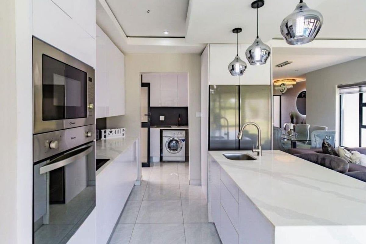 Modern kitchen featuring a central island with stone countertops, integrated appliances, sleek cabinetry, and tiled flooring, leading into a separate laundry area.