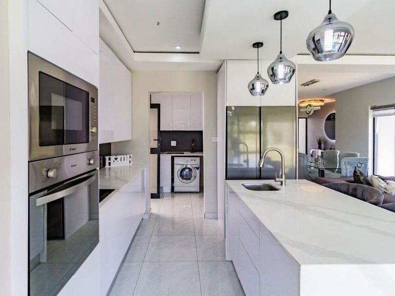 Modern kitchen featuring a central island with stone countertops, integrated appliances, sleek cabinetry, and tiled flooring, leading into a separate laundry area.