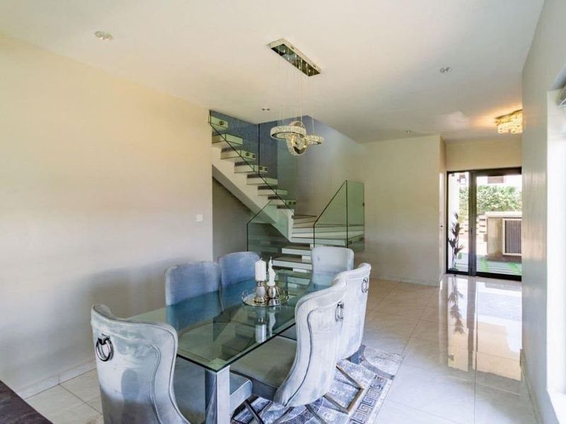 Modern dining area featuring tiled flooring, recessed lighting, and a contemporary staircase with a glass balustrade leading to the upper level.