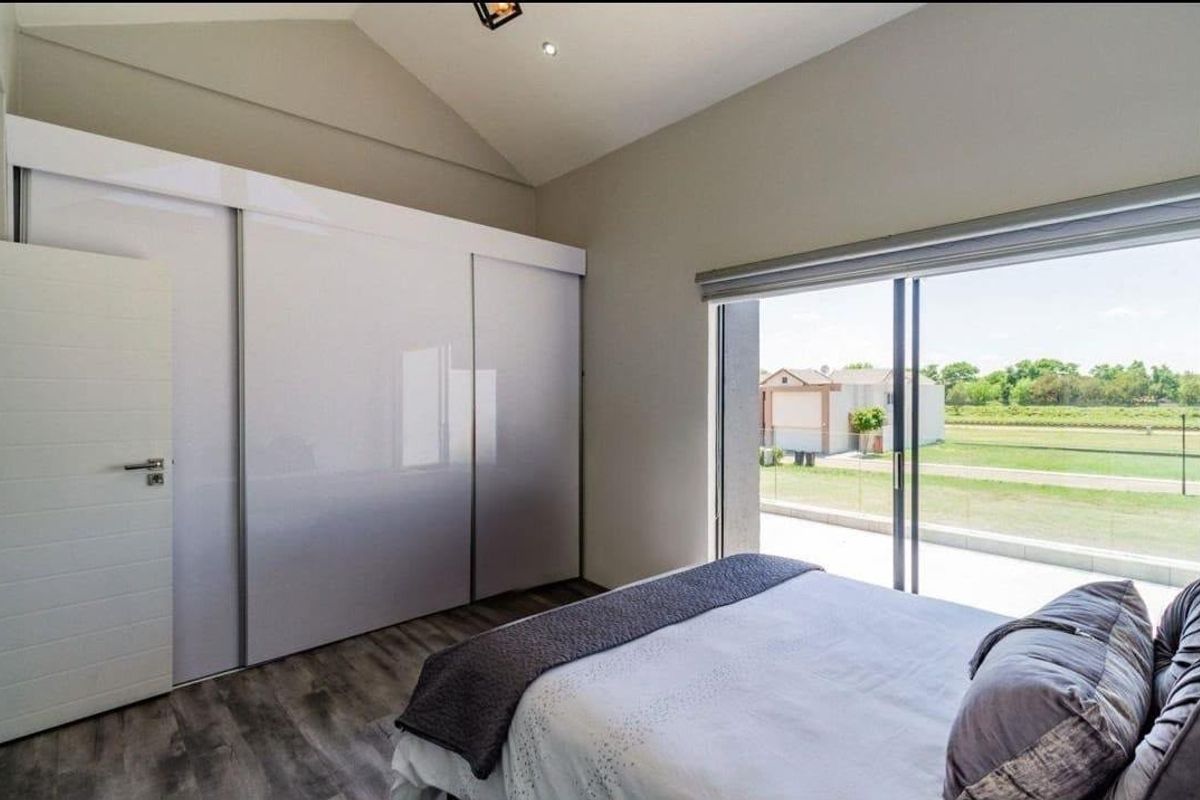 Modern bedroom featuring vaulted ceilings, built-in high-gloss sliding wardrobes, laminate flooring, and large sliding glass doors opening to an outdoor area.