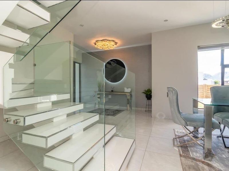 Modern living area featuring a striking floating staircase with glass balustrades, polished tiled flooring, and contemporary lighting fixtures.