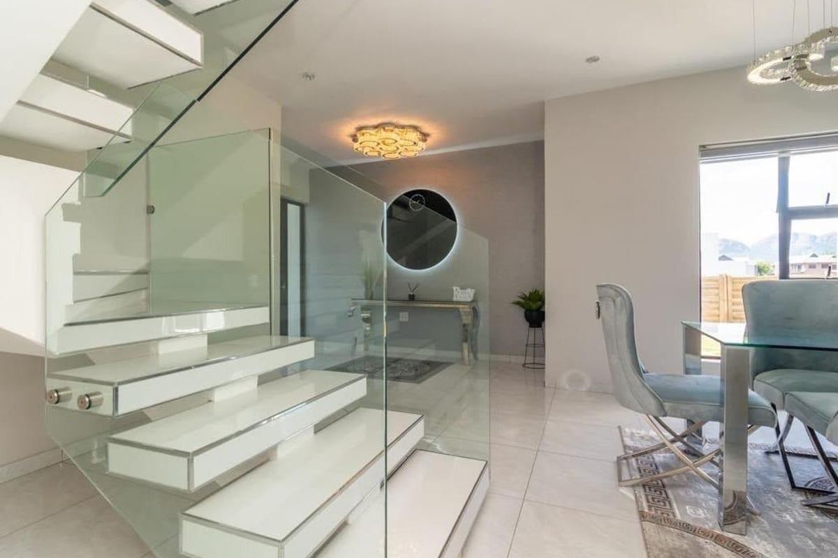 Modern living area featuring a striking floating staircase with glass balustrades, polished tiled flooring, and contemporary lighting fixtures.