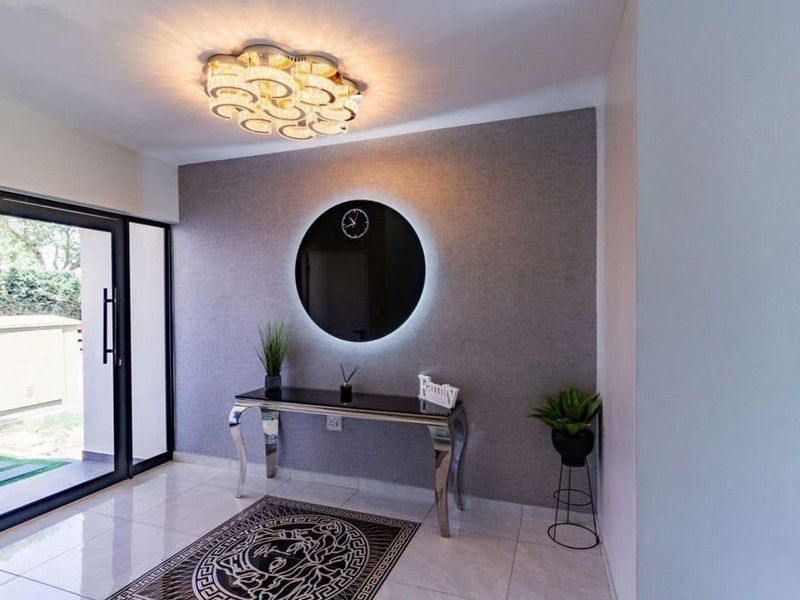 A modern, well-lit entrance hall featuring tiled flooring, a decorative feature wall, and a large sliding glass door providing access to the exterior.