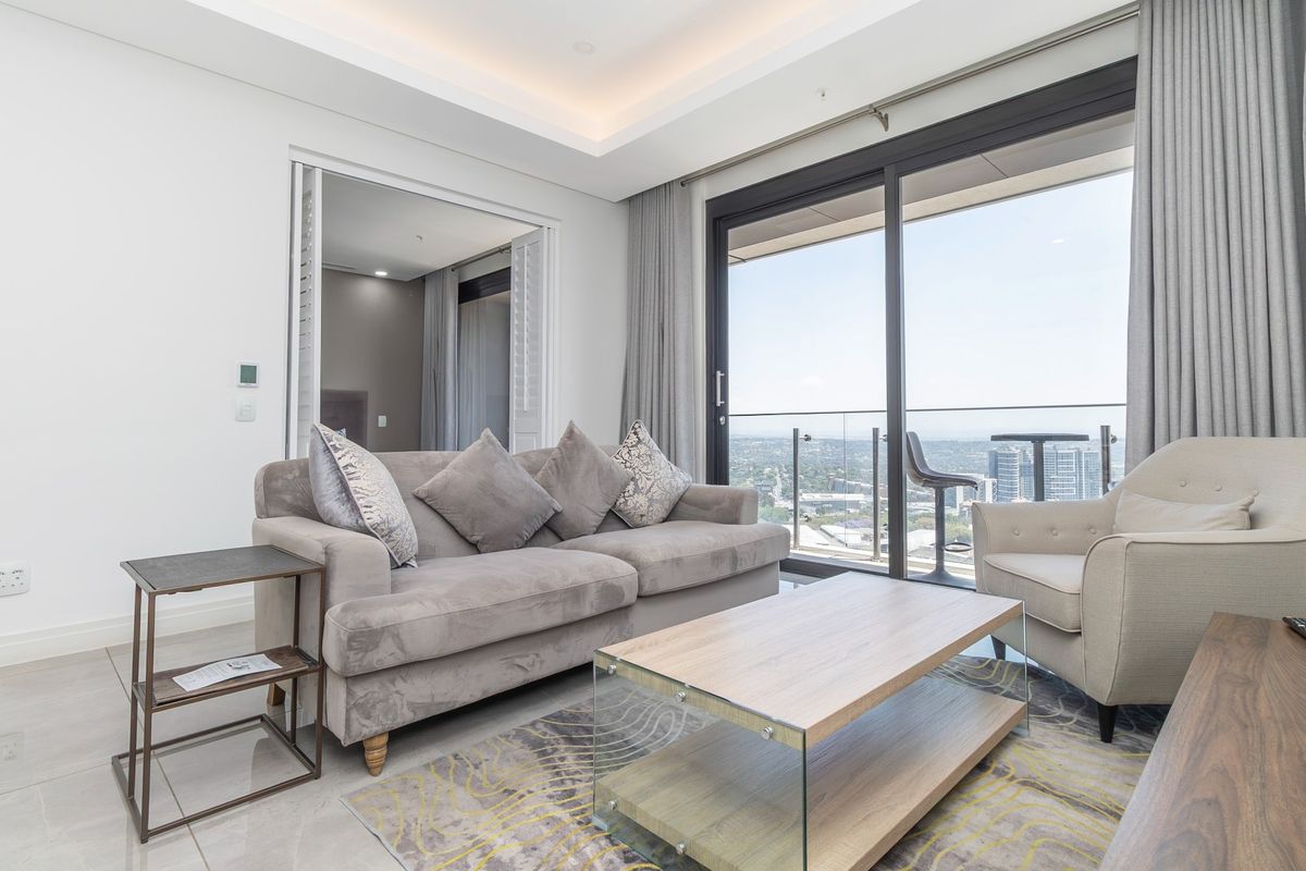 Modern living room featuring recessed ceiling lighting, tiled floors, and large sliding glass doors opening to a balcony with expansive city views.