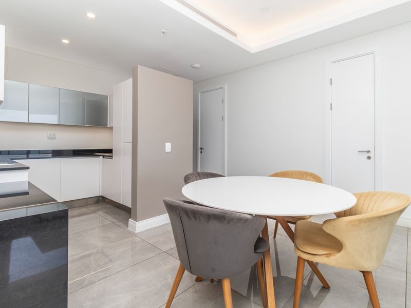 Modern open-plan kitchen and dining area featuring sleek cabinetry, stone countertops, polished tile flooring, and elegant recessed ceiling lighting.