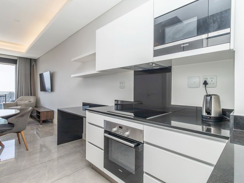 Modern open-plan kitchen featuring sleek white cabinetry, black stone countertops, integrated Siemens appliances, and polished tile flooring, seamlessly flowing into the living area.